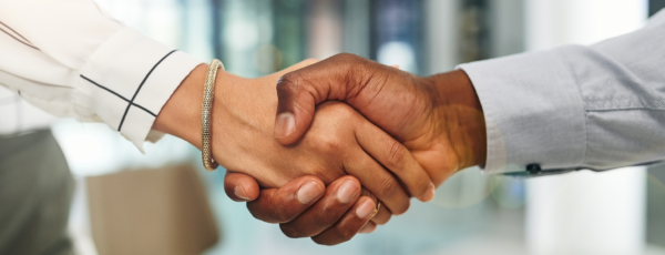 A close-up of two people shaking hands, symbolizing agreement or partnership. The person on the left wears a bracelet and the person on the right wears a shirt.